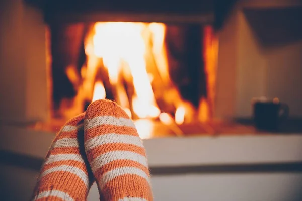 Feet in wool striped socks by the fireplace. Relaxing at Christmas fireplace on holiday evening. — Stock Photo, Image