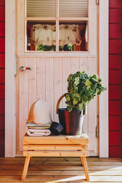 Sauna accessories with birch broom, hat and towels near a red wooden sauna in Finland — ストック写真