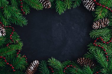 Karanlık arka planda ladin dalları, koniler ve kırmızı çelenklerle Noel düzeni. 