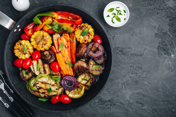 Овощное блюдо на гриле с цуккини, грибами, баклажанами, морковью, перцем, помидорами, луком, кукурузой и мятным соусом йогурта. Вид сверху
.