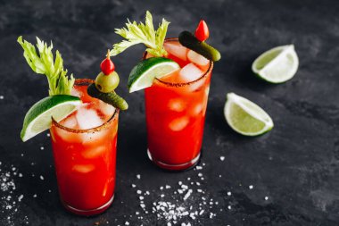 Süslü bardakta Bloody Mary kokteyli. Taze kereviz, turşu ve koyu arkaplanda limon ile buzlu domates suyu. Boşluğu kopyala..