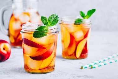 Ev yapımı şeftalili buzlu çay ya da taze naneli limonata ve gri taş arka planda cam kavanozda buz küpleri..