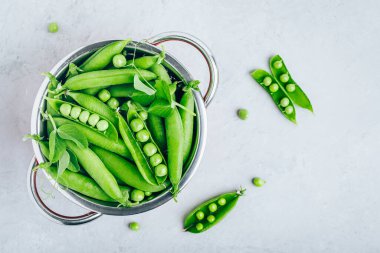 Gri taştan arka planda kevgirde taze taze taze bezelyeler, üst görünüm