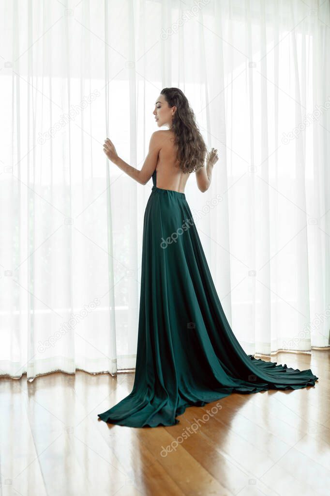 Beautiful girl with long curly hair posing in a beautiful evening dress with an open back.