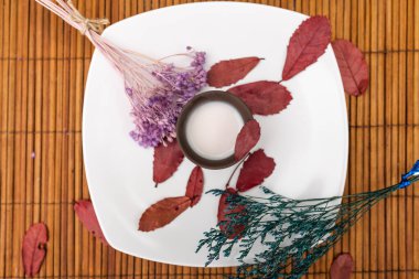 Süt ve lavanta filizi ve kırmızı ağaç yapraklarıyla dolu kilden bir bardağın üzerine yerleştirilmiş beyaz bir tabak..