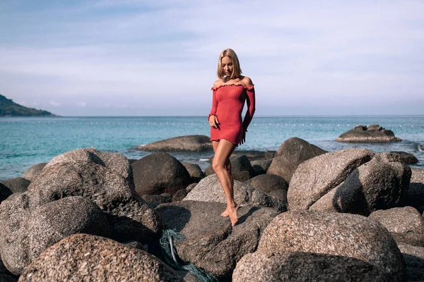 Retrato de Joven hermosa rubia en vestido rojo ajustado de pie sobre roca en el mar azul.Sentirse bien, libre, feliz. Verano, cálido, buen tiempo. Phuket. Tailandia — Foto de Stock