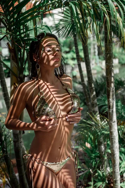 Sexy brunette posing standing among palm leaves — Stock Photo, Image