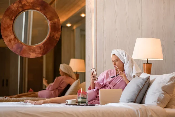Όμορφη γυναίκα με πετσέτα στο κεφάλι να μιλάει στο τηλέφωνο στην κρεβατοκάμαρα στο σπίτι. Πρωινή ρουτίνα — Φωτογραφία Αρχείου