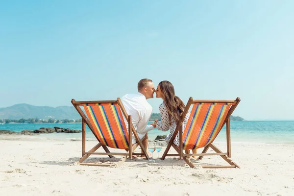 Romantik tatil seyahati. Gün batımında deniz kenarında lüks sahil otelinde güverte sandalyeleriyle sarılan mutlu genç çiftin portresi.. — Stok fotoğraf