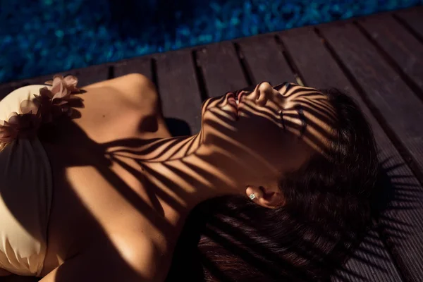 Barevný letní portrét mladé atraktivní brunetky se zavřenýma očima pod palmou u bazénu — Stock fotografie