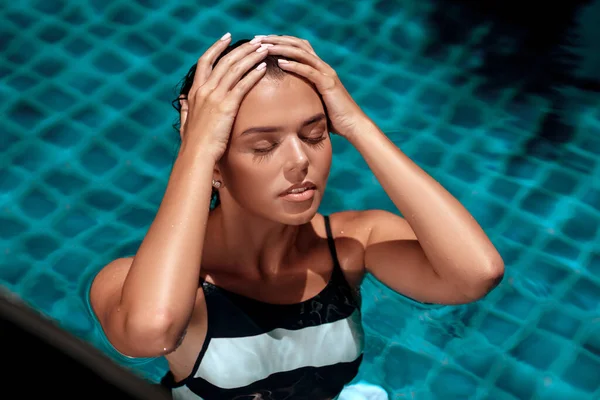 Chica de belleza bronceada en un traje de baño a rayas de moda acostado en el agua de la piscina con los ojos cerrados. Spa y concepto de relajación. Vacaciones de verano — Foto de Stock