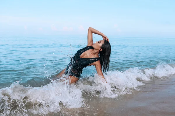 Charmante Miss im eleganten schwarzen Badeanzug und hellem Make-up liegt und entspannt am Strand. — Stockfoto