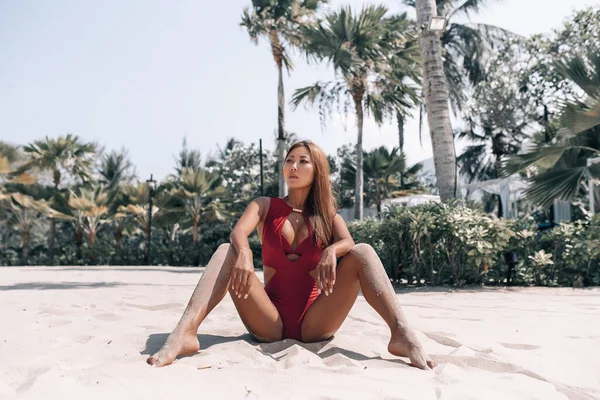 Sexy schöne asiatische Frau am Strand Sommerurlaub in einem modischen roten Bikini sitzt auf Sand im Urlaub. — Stockfoto