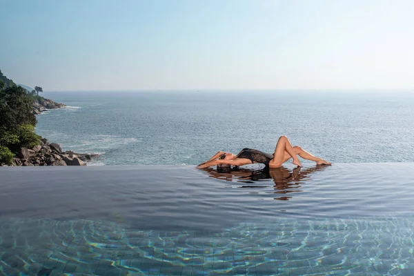 Slender beautiful blonde relaxes in the infinity pool at the resort — Stock Photo, Image
