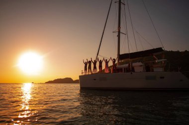 Bir grup arkadaş gün batımında bir yatta el ele tutuşuyorlar..