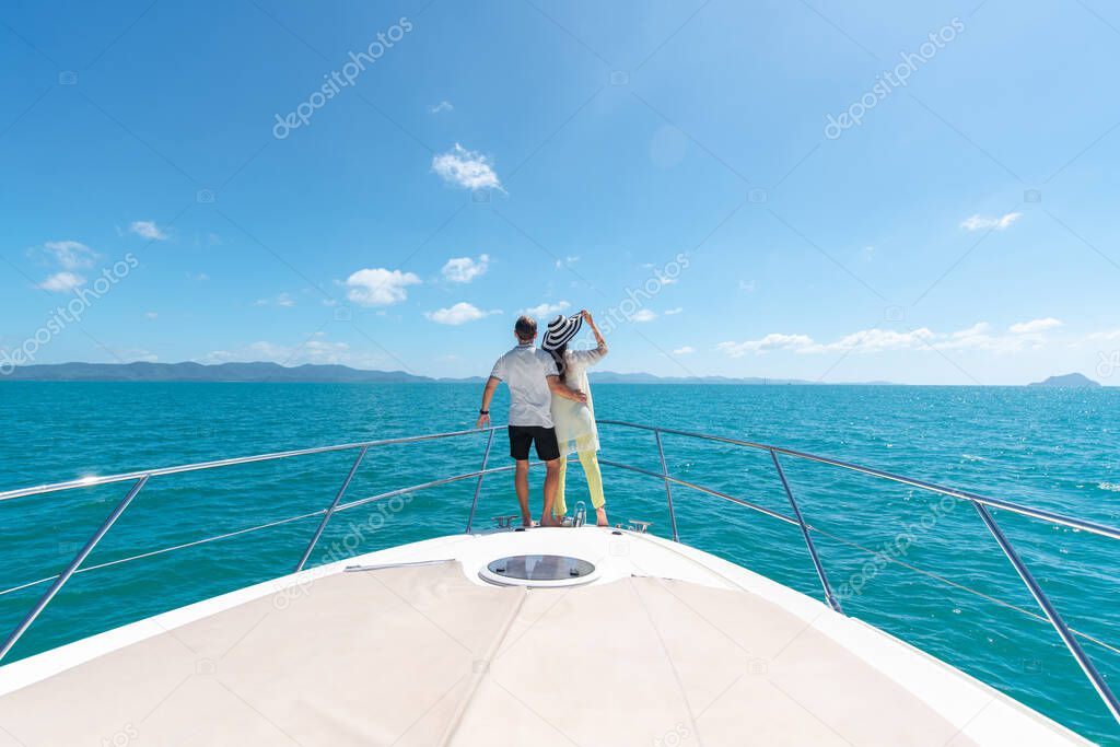 Back view of a sweet couple standing on edge of luxury yacht. Brunette wearing straw hat and fashion summer suit and sunglasses. Luxury seascape