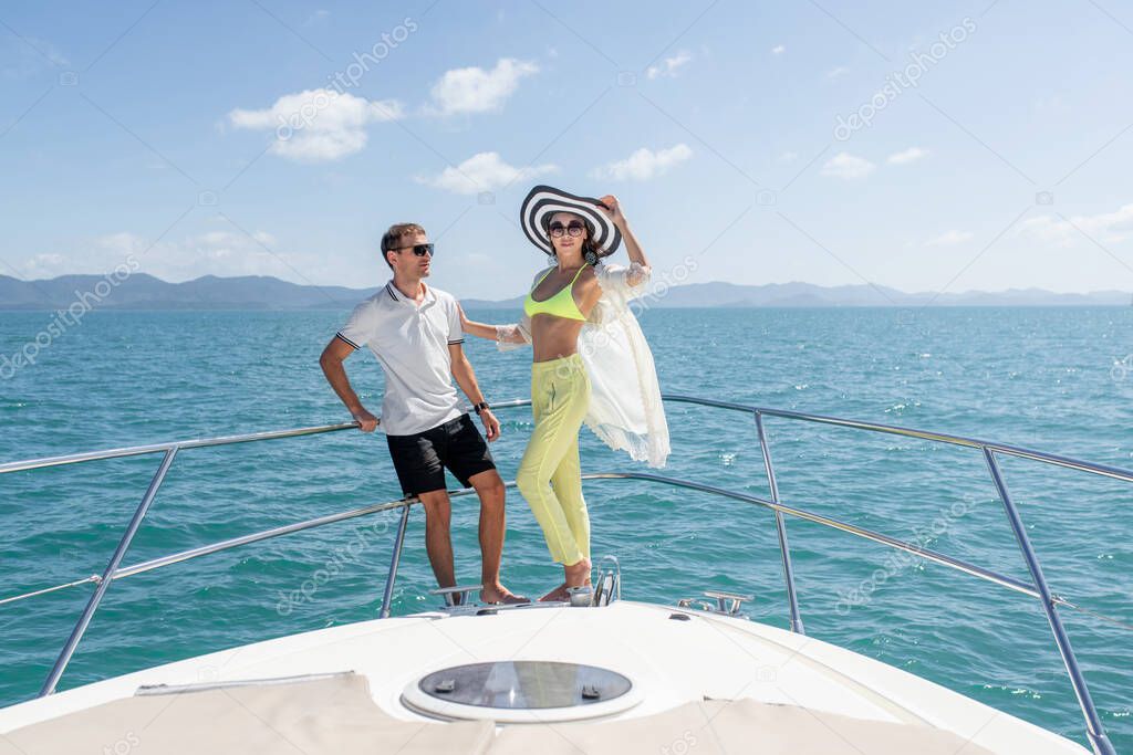 sweet couple standing on edge of luxury yacht. Brunette wearing straw hat and fashion summer suit and sunglasses.