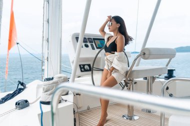 Çekici ve muhteşem esmer, modern bir motorlu teknede oturuyor ve sürüyor. Sevimli kız rahatlıyor ve kameraya poz veriyor. Siyah bikini giyen bir manken. Lüks yaz tatili