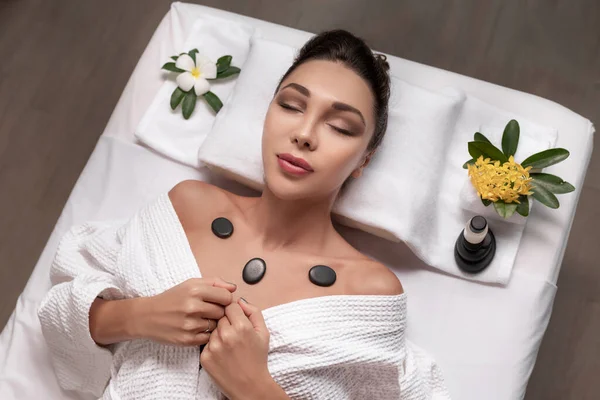 Woman Closed Eyes White Bathrobes Relaxing Massage Table Hot Stones — Stock Photo, Image