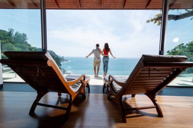 Terasta iki güneşli yatak, yakın plan. Sevgi dolu bir çift şeffaf bir balkondaki deniz manzarasına bakar. Arka plan