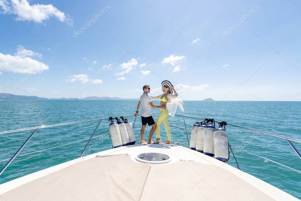 Love and travel concept. Sweet couple standing on edge of luxury yacht. Brunette wearing straw hat and fashion summer suit and sunglasses.