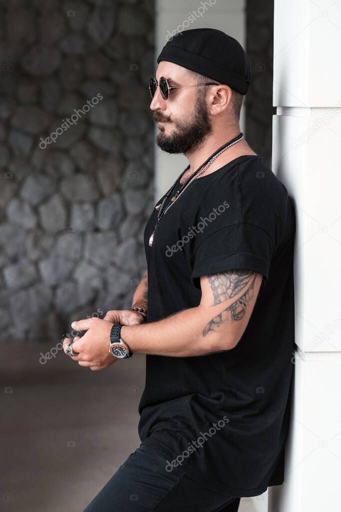 Profile photo: a stylish brutal man in black clothes with a beard and mustache stands near the wall