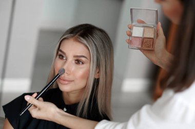 Makyaj sanatçısı makyajını yapıyor, makyaj fırçasıyla yüz pudrasını uyguluyor.