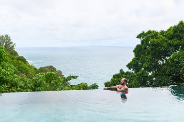 Sakallı ve bıyıklı yakışıklı bir adam sonsuz bir havuzun kenarında rahatlıyor. Lüks deniz manzarası.