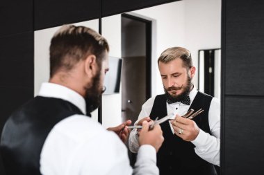 Zarif bıyıklı bir adam aynanın yanında tıraş olmadan önce bıçağı inceler.