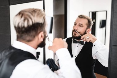 Adam aynanın önündeki lüks bıyığını kesiyor.