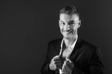 Gömleğinin düğmelerini açmış takım elbiseli gülümseyen bir adamın siyah beyaz portresi..