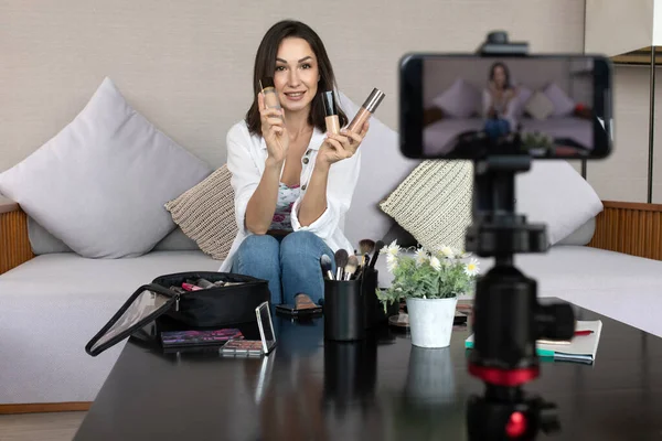 Young lady talking on cosmetics holding a tonal foundation while recording her video. Woman making a video for her blog on cosmetics.