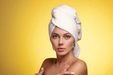 Kafasında havlu olan ve makyajlı çekici genç bir kadın, sarıda soyutlanmış.