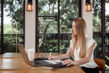 Yetenek ve bilgiyi geliştirmek için webinar izleyerek yaratıcı bir iş üzerinde çalışan konsantre sarışın kadın metin yazarı, laptop bilgisayar kullanarak web sitelerinde son haberleri izleyen çekici gazeteci