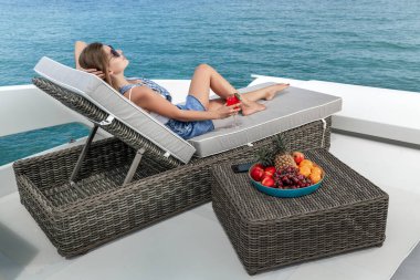 Yan manzara: lüks bir kadın güneşli bir yatakta uzanıyor, karpuz suyu içiyor bir yaz gezisi sırasında yatta yelken açıyordu. Yanındaki tabakta tropik yaz meyveleri.