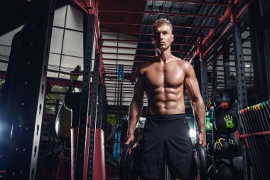 Spor salonunda ağırlık kaldıran çıplak kaslı yakışıklı bir adam..