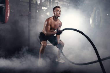 Spor salonunda ip sallayarak çapraz atak egzersizi yapan beyaz bir genç. Dumanlı spor salonundaki egzersiz kavramı.