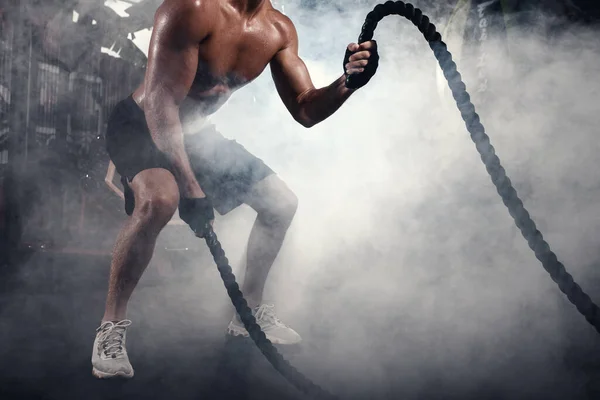 Close up of athletic man doing crossfit exercises with rope in smoky gym