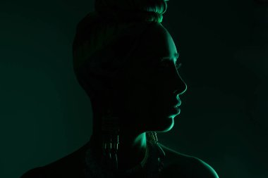 Kafasında eşarp ve kocaman küpeler olan doğulu bir kadının profil fotoğrafı. Fotoğraf karanlıkta çekilmişti.