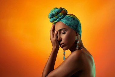 Doğulu muhteşem bir kadın yüzünün yarısını eliyle kapatıyor. Etnik tarzda. Aksesuarlar ve parlak makyaj.