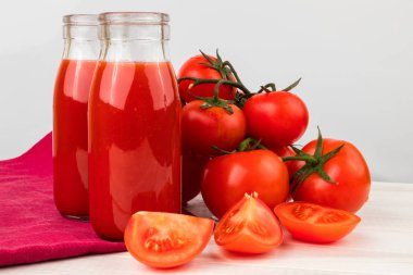 Hafif ahşap masada Taze Olgun Domates ile Domates Suyu İki Şişe. 