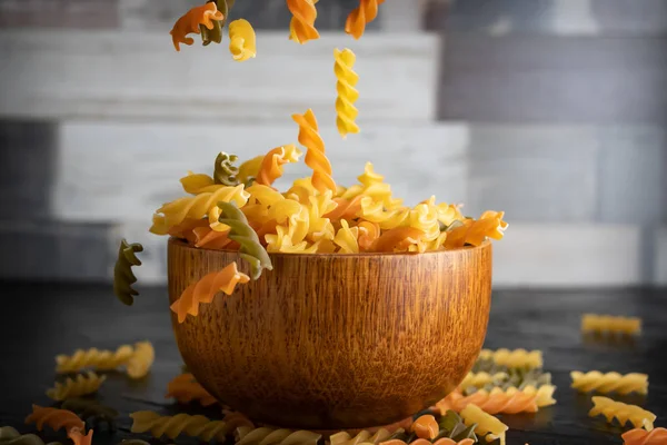 Uncooked Pasta Fusilli falling in a wooden bowl on a blurred background. Close-up