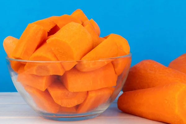 Fresh chopped carrots in a glass bowl on a blue background
