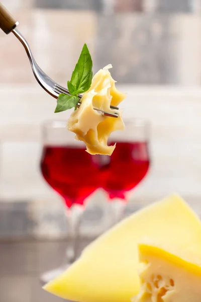 A piece of cheese on a fork close-up on a background of two glasses with red wine