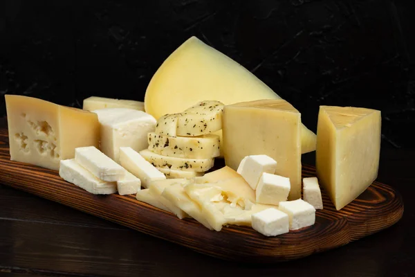 Koyu bir arka plan üzerinde ahşap kesme tahtası üzerinde peynir farklı türleri