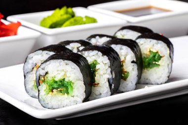 Siyah bir arka planda beyaz bir tabakta yosun ve susam tohumlarıyla yuvarlan. Suşi menüsü. Japon yemeği..