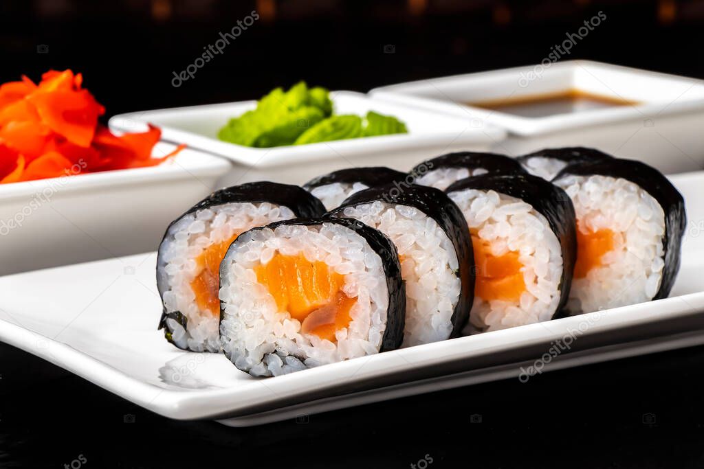 Rolls with salmon on a white plate on a dark background. Sushi menu. Japanese food.
