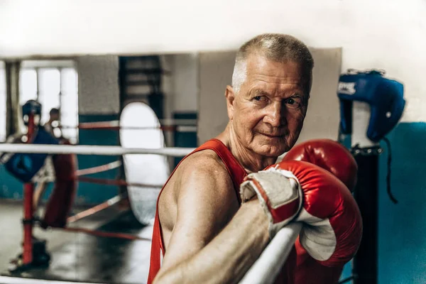 Happy funny senior boxer man with red gloves in the ring