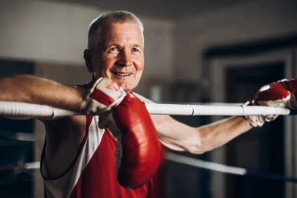 Happy funny senior boxer man with red gloves in the ring