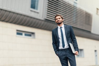 Elinde dizüstü bilgisayar la takım elbiseli işadamı cam ofis binasının girişine giden yolda işe gidiyor.